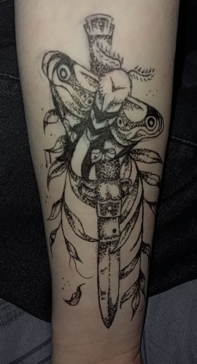 A drawing of a moth on a knife with ferns in a background on a person's arm